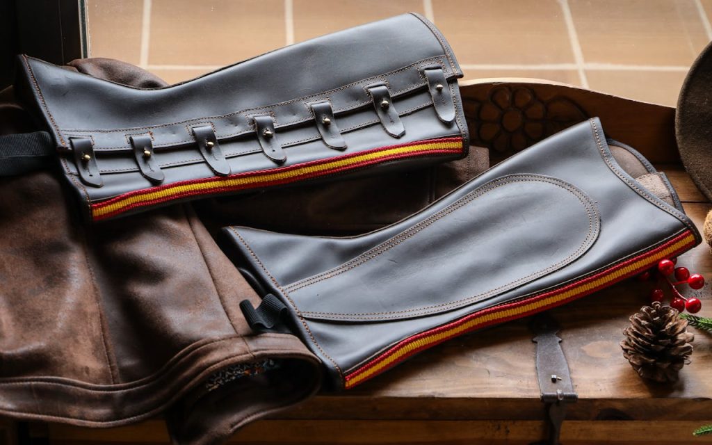 Leather chaps with vibrant trim placed on rustic surface, capturing equestrian style.